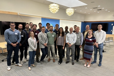 A group of about 20 people pose standing at MIT.nano.