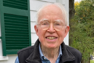 Photo of Fred Greene standing outdoors, weFred Greene stands in front of a white house, wearing an MIT Chemistry fleecearing his MIT Chemistry fleece