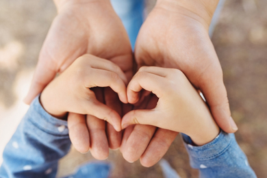 Child’s hands make a heart-shape above adult’s hands.