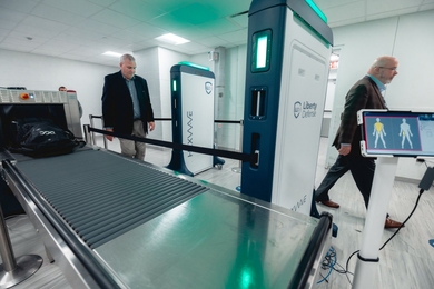 Two individuals walk past a security screening system. 