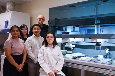 Five people wearing eye protection pose near a workbench in a biological laboratory