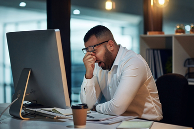 A tired man yawning in front of his computer
