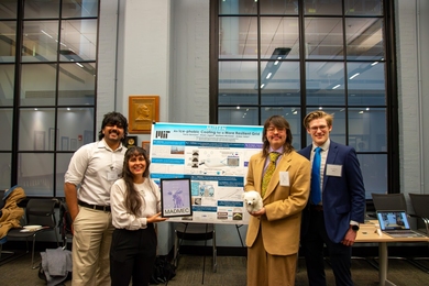 Four MIT students pose in front of a scientific poster, two on each side. One holds the team’s framed first-place award. 