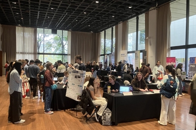 Students mill about a large room with numerous staffed tables with black tablecloths.