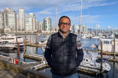 Badri Ratnam stands in front of a marina with buildings and water in the background