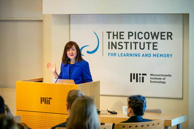 Li-Huei Tsai speaks at a lectern with an MIT logo. Behind her is the Picower Institute logo.