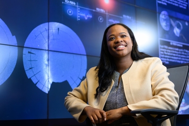 Carissma McGee poses seated in front of a blue wall with out-of-focus text and diagrams