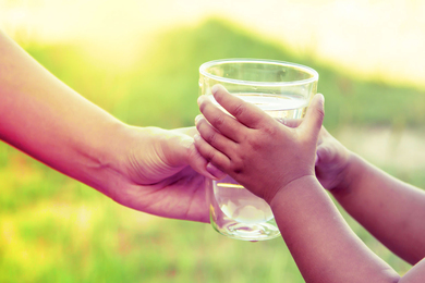 A person hands a glass of water to a child.