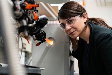 Desirée Plata in the lab wearing safety goggles and leaning over a machine.