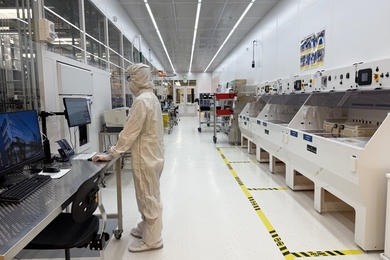 A person in a bunny suit stands at a computer in a cleanroom.