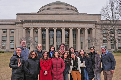 14 MIT graduate students and AP collaborators pose in front of the MIT dome on a cloudy day in late winter
