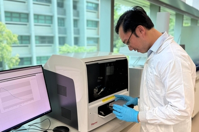 Mervin Ang places a sample inside a machine resembling a desktop microwave oven