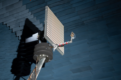 An antenna with 256 small, square elements in a 16x16 grid is held up in an anechoic chamber. 