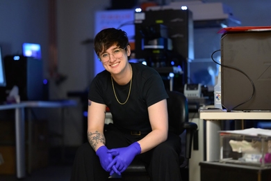 Shannon Knight, wearing nitrile gloves, poses in a chair in her lab