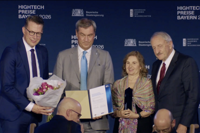Daniela Rus stands on stage with three colleagues. One holds a floral bouquet and another displays an opened award folder